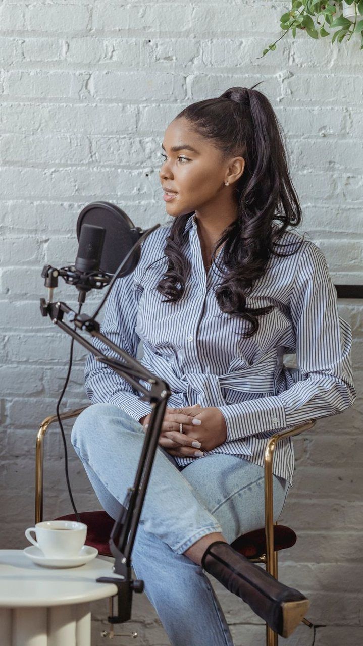 Vertical clip of a woman seated at a podcast mic in a bright studio
